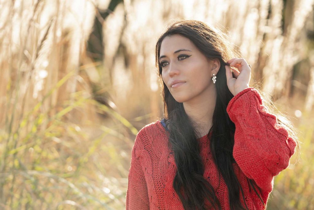 A young woman in a red seater poses during golden hour sunlight